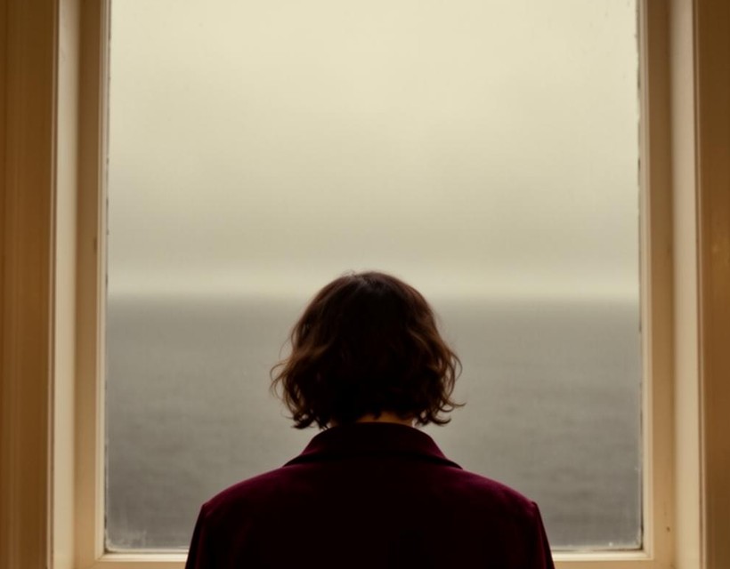 A woman gazing toward a quiet horizon at dusk in warm light