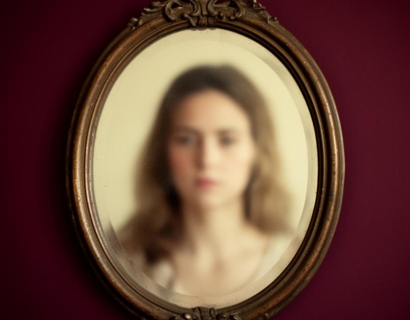 A softly blurred reflection of a woman in an old mirror