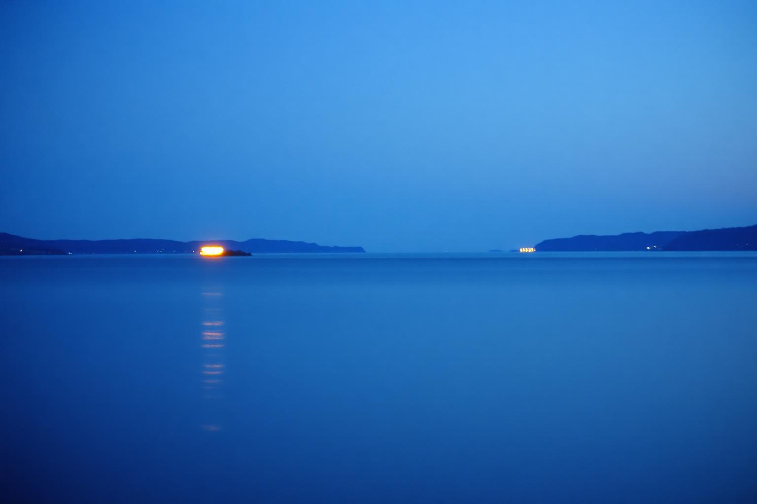 Two distant lights on opposite shores of a dark calm bay at night.