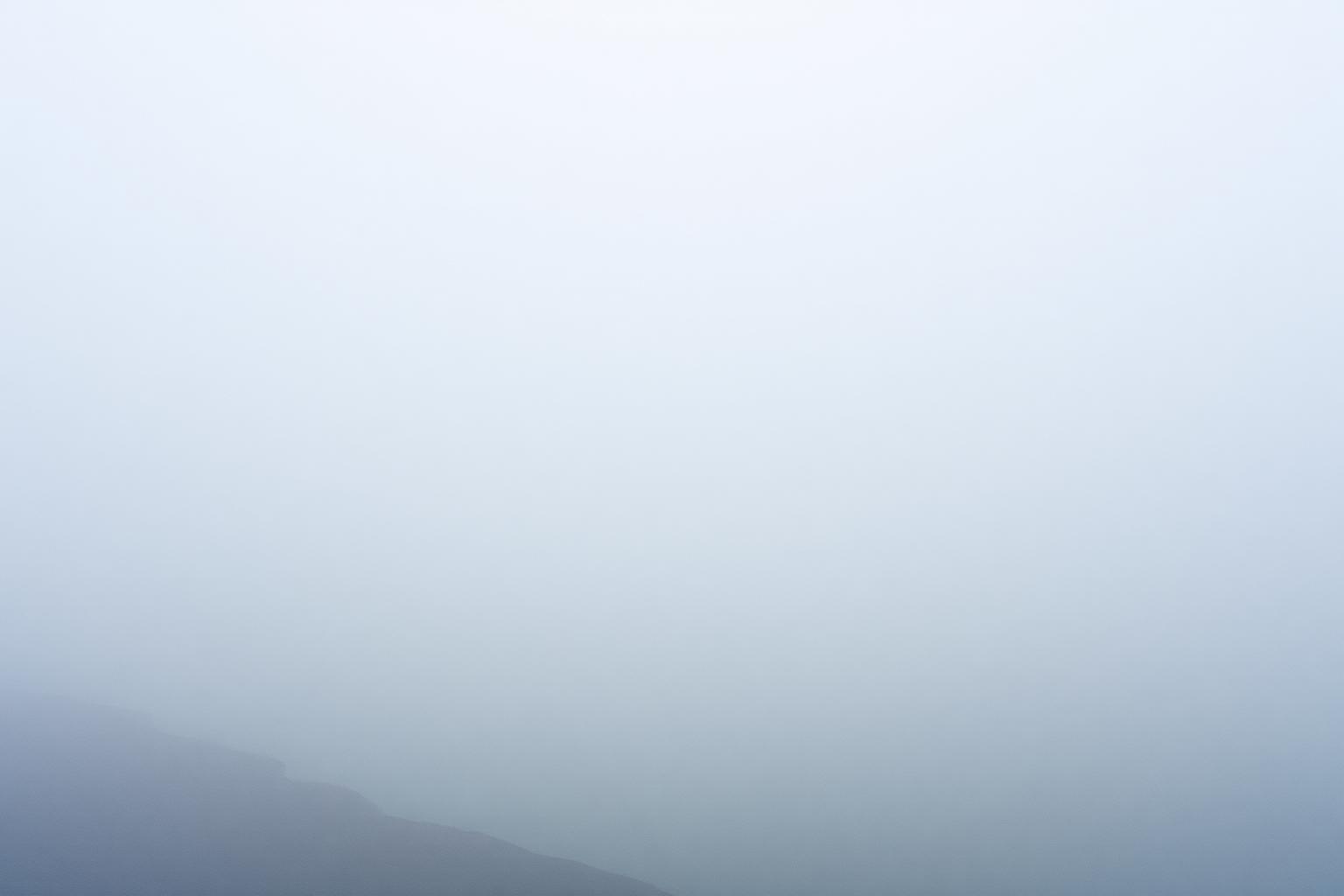 A foggy shoreline where the water and sky blur into a single pale grey.